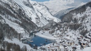 A snow-covered mountain village with a lake, surrounded by forested slopes and snow-capped peaks.