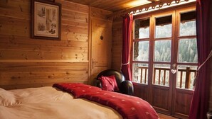 A wooden cabin room with a bed, a chair, and a large window with curtains.