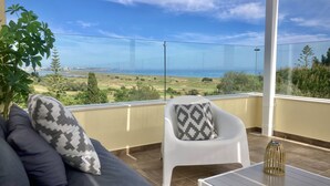 A balcony with a sofa and armchair, a table, and a view of a coastal landscape. - ❀Family Paradise. Peaceful, golf, countryside & beach, pool, close to everything (Lagos)