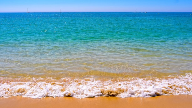 A beach with clear turquoise water, gentle waves, and a distant sailboat. - ❀Family Paradise. Peaceful, golf, countryside & beach, pool, close to everything (Lagos)