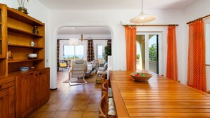 A spacious living area with a wooden dining table, a sofa, and a chair. There is a large window with curtains, a hanging light fixture, and a view of the outdoors. - ❀Family Paradise. Peaceful, golf, countryside & beach, pool, close to everything (Lagos)