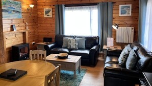 A cozy cabin interior with wooden walls, a black leather sofa, a wooden coffee table, and a fireplace. - Willow Lodge, Holiday Log Cabin, Cedar Springs, Heacham. Close to the beach. (Heacham)