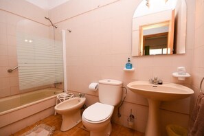 Un bagno dotato di vasca, due servizi igienici, un bidet, un lavandino e uno specchio.