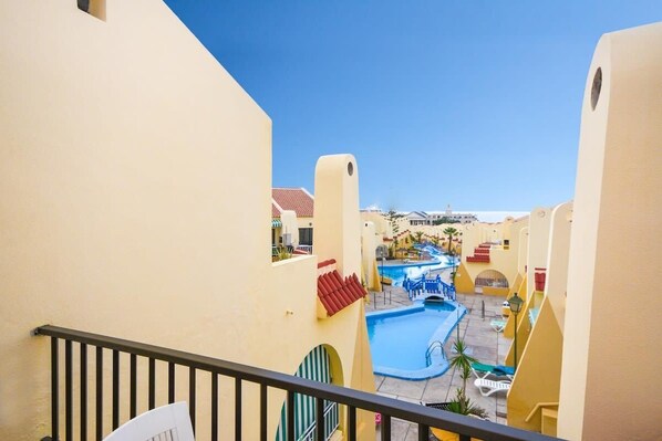 Cortile di un hotel con diverse piscine, uno scivolo acquatico al centro e un cielo azzurro terso.