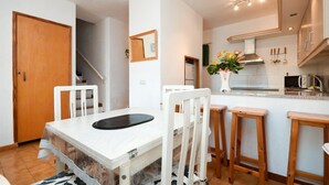 Une cuisine moderne avec des meubles blancs, un four encastré et un coin repas comprenant une table et des chaises blanches.