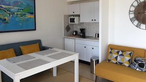A compact living space with a kitchenette, a dining table, a sofa, and a large abstract painting.