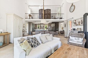 A spacious living area with a sofa, a dining table, and a balcony with a railing. - LARGE HOUSE, GORDES , heated swimming pool , view over Goult, Roussillon (Joucas)