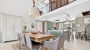A spacious dining area with a wooden table and chairs, a hanging light fixture, and a view of the kitchen and upper floor. - LARGE HOUSE, GORDES , heated swimming pool , view over Goult, Roussillon (Joucas)