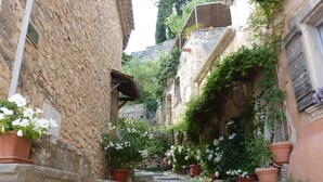 A narrow cobblestone street flanked by stone buildings with potted plants and flowers. - LARGE HOUSE, GORDES , heated swimming pool , view over Goult, Roussillon (Joucas)