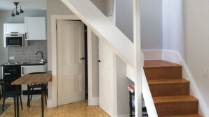 A modern kitchen with white cabinets, a microwave, and a sink. There is a wooden dining table with chairs. A white door leads to a staircase. - Cottage in the Highest Village in Scotland (Wanlockhead)