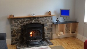 A cozy living room with a stone fireplace, a mounted television, and a rustic wall art piece. - Cottage in the Highest Village in Scotland (Wanlockhead)