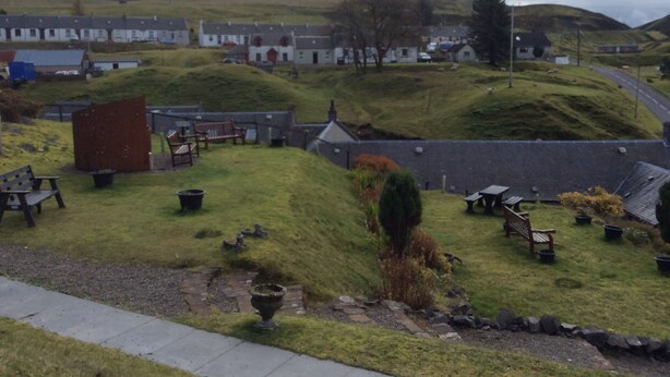 A rural landscape with rolling hills, a small village, and a few benches and tables in a grassy area. - Cottage in the Highest Village in Scotland (Wanlockhead)