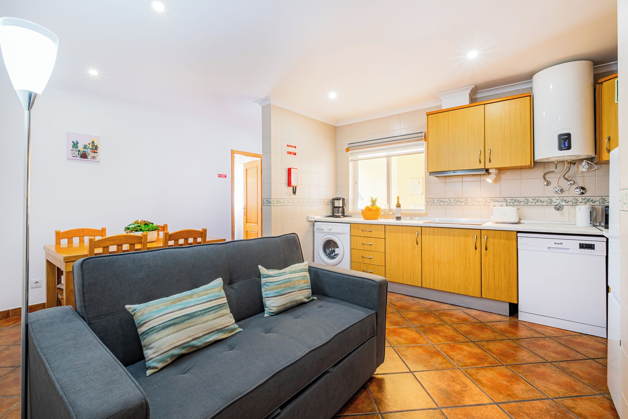A compact living space with a sofa, a dining table, and a kitchen area including a washing machine and a water heater.