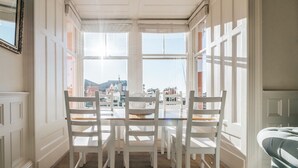 A dining area with a table and chairs, large windows, and a view of buildings outside. - Luxury Seafront Apartment in Aberdovey -pets allowed/free parking -sleeps 8 (Aberdovey)