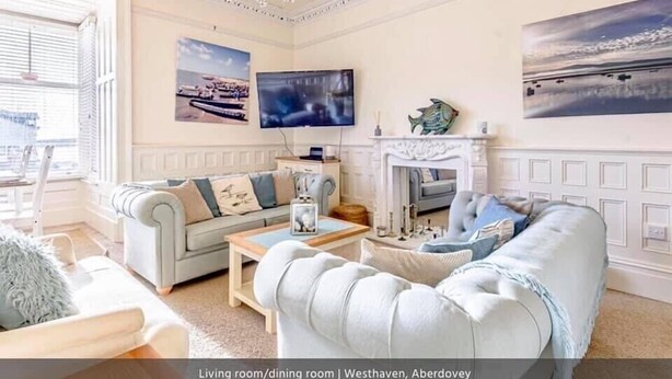 A living room/dining room with a chandelier, a fireplace, a television, and artwork on the walls. - Luxury Seafront Apartment in Aberdovey -pets allowed/free parking -sleeps 8 (Aberdovey)