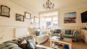 A well-lit living room with a large window, a chandelier, and a view of the outside. - Luxury Seafront Apartment in Aberdovey -pets allowed/free parking -sleeps 8 (Aberdovey)
