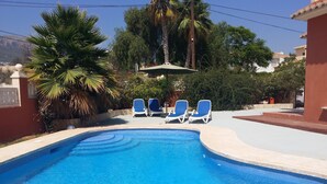 A swimming pool with blue water, surrounded by a tiled deck. There are three blue lounge chairs and a white umbrella. - Casa Feli. Luxury apartment in villa. Large terrace. Private entrance. AC. (Calp)
