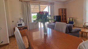 Un comedor con una mesa de madera, sillas, un jarrón con flores, un televisor y un aparador.