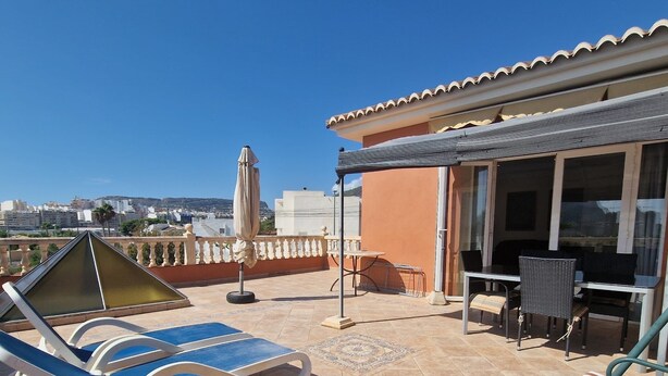 Una terraza en la azotea con sillones, una mesa y un área techada con vistas a la ciudad.
