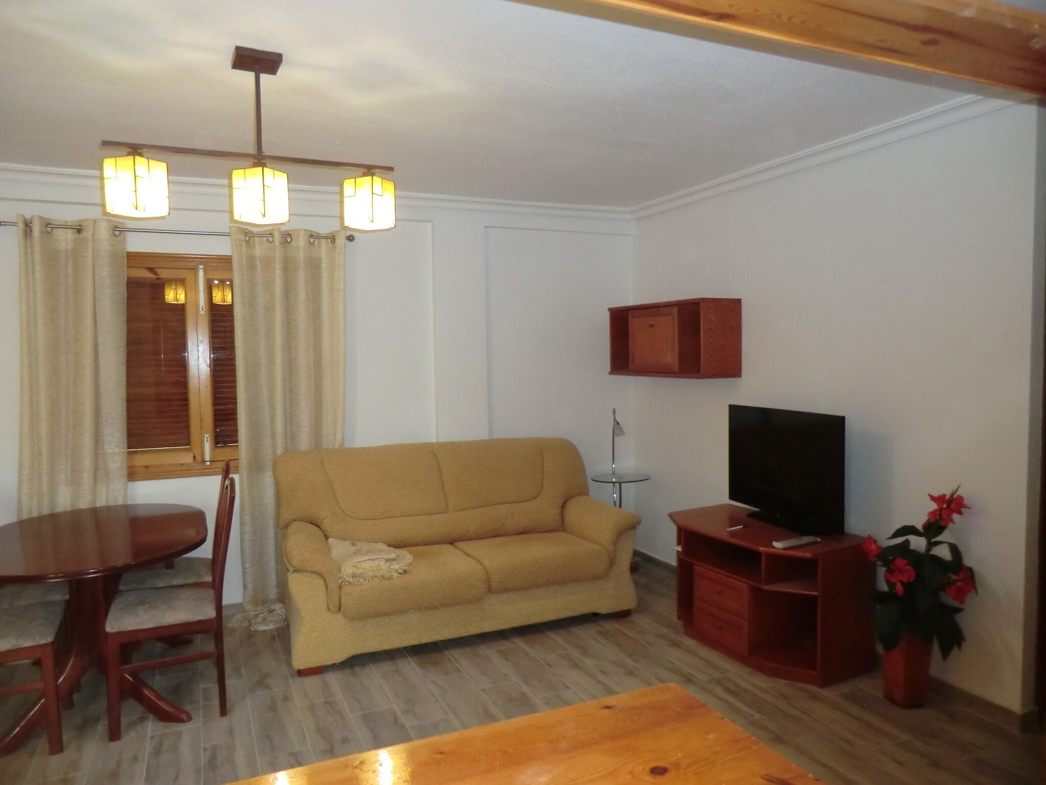 Un salon comprenant un canapé, un téléviseur, une table basse en bois, une table à manger avec des chaises et une fenêtre avec des rideaux.
