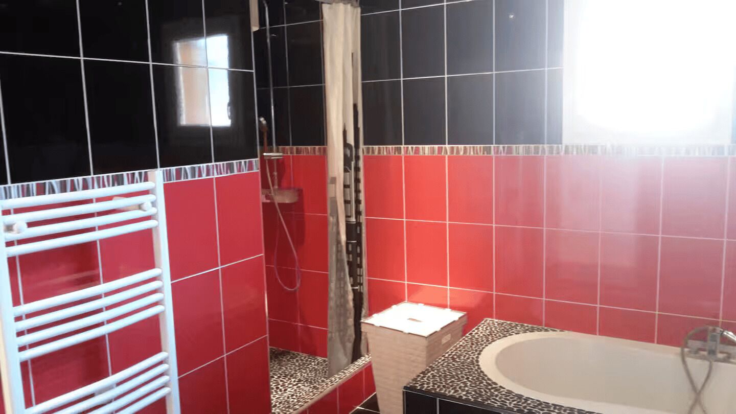 A bathroom with red and black tiles, a shower, a bathtub, and a towel rack.