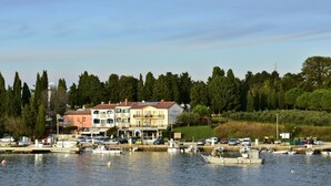 Un puerto deportivo con barcos amarrados, un edificio frente al agua con varios pisos, y un fondo de árboles.
