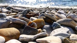 Una playa de guijarros con un muelle al fondo.