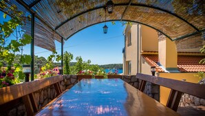 An outdoor dining area with a wooden table and chairs, surrounded by stone walls and potted plants. - Nice and fresh two with sea views, large balcony and pool access. (Rab)
