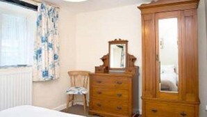 Een slaapkamer met een bed, een houten dressoir, een stoel en een grote spiegel.