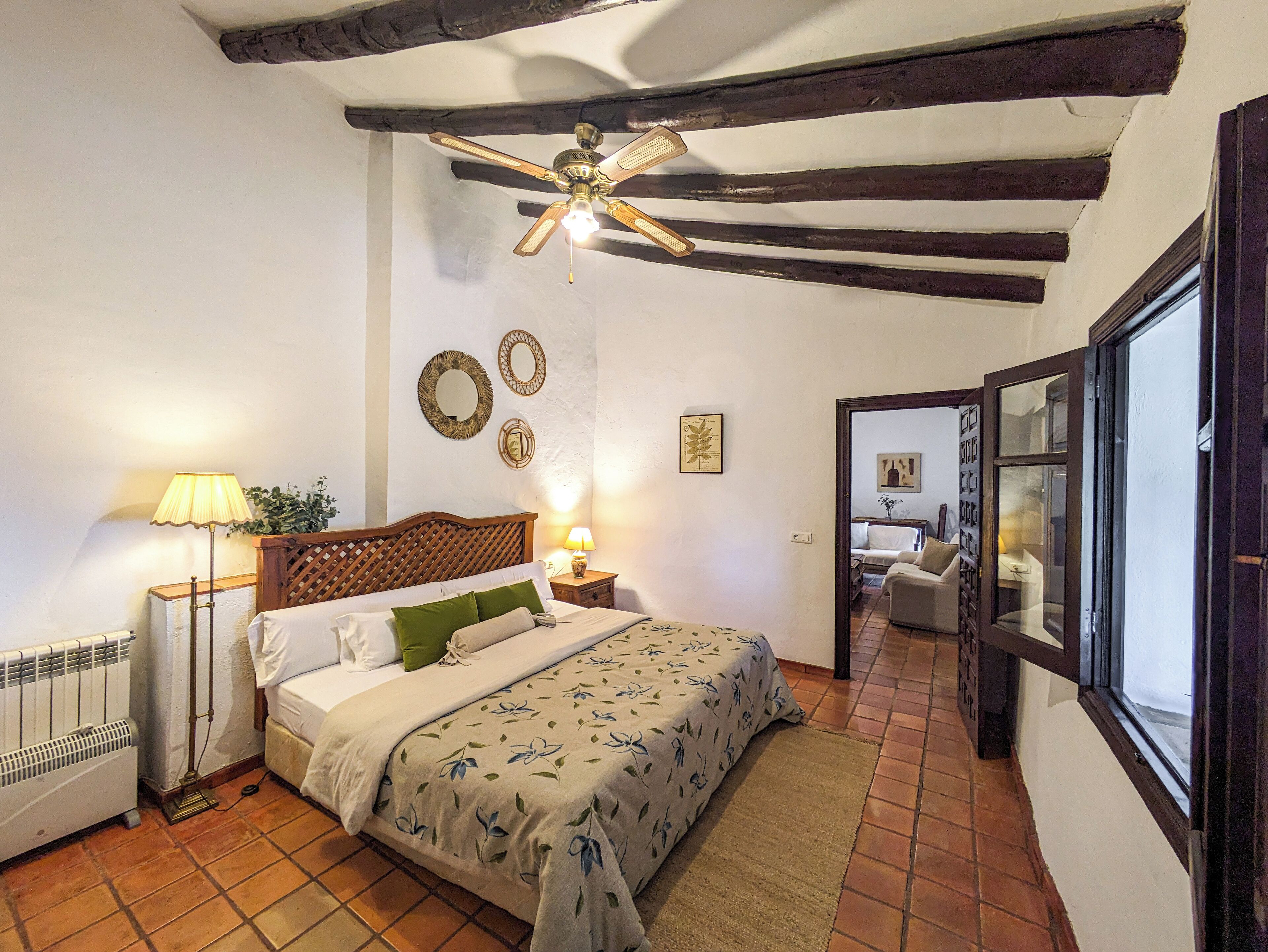A bedroom with a bed, a radiator, a ceiling fan, and a view of another room through an open door.