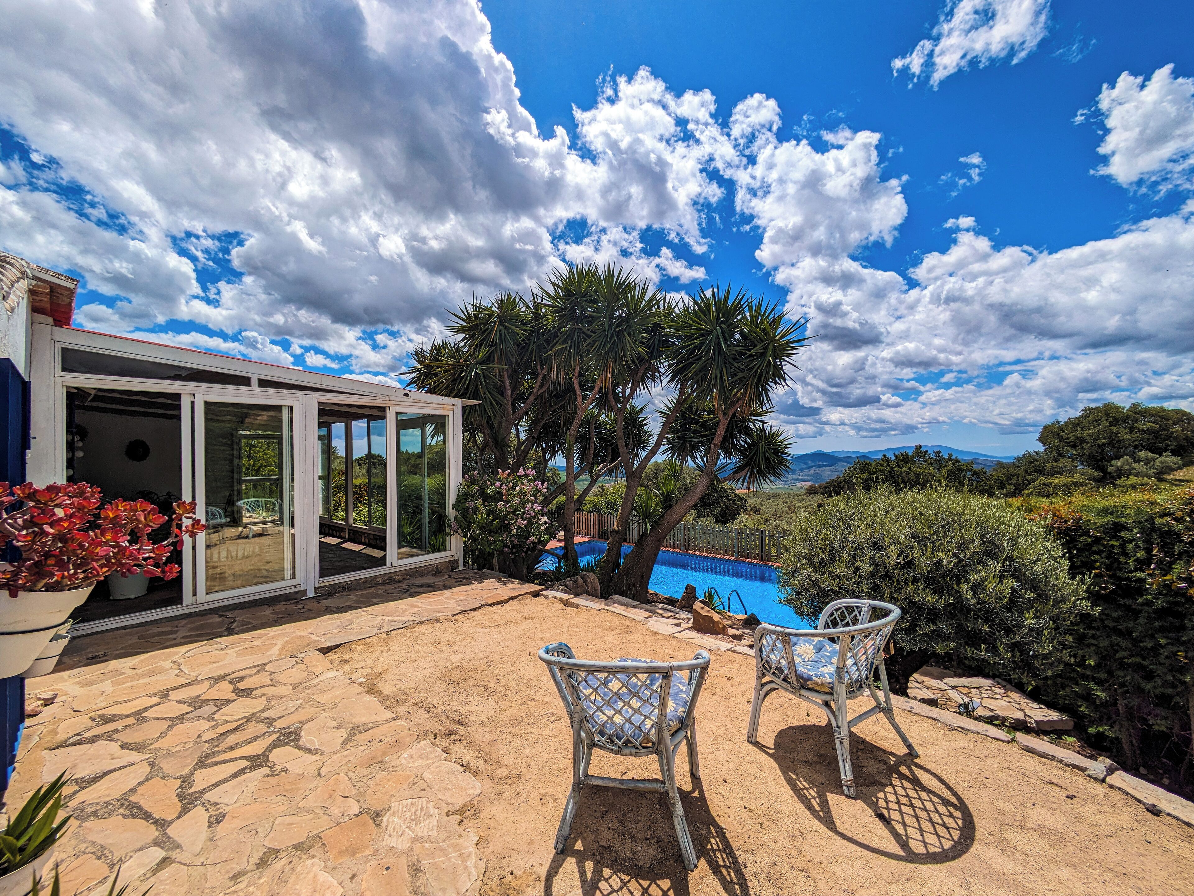 A patio with two wicker chairs, a glass-enclosed structure, and a view of the landscape.