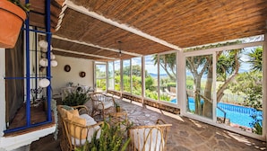 A covered patio with wicker furniture, a stone floor, and a view of a swimming pool.
