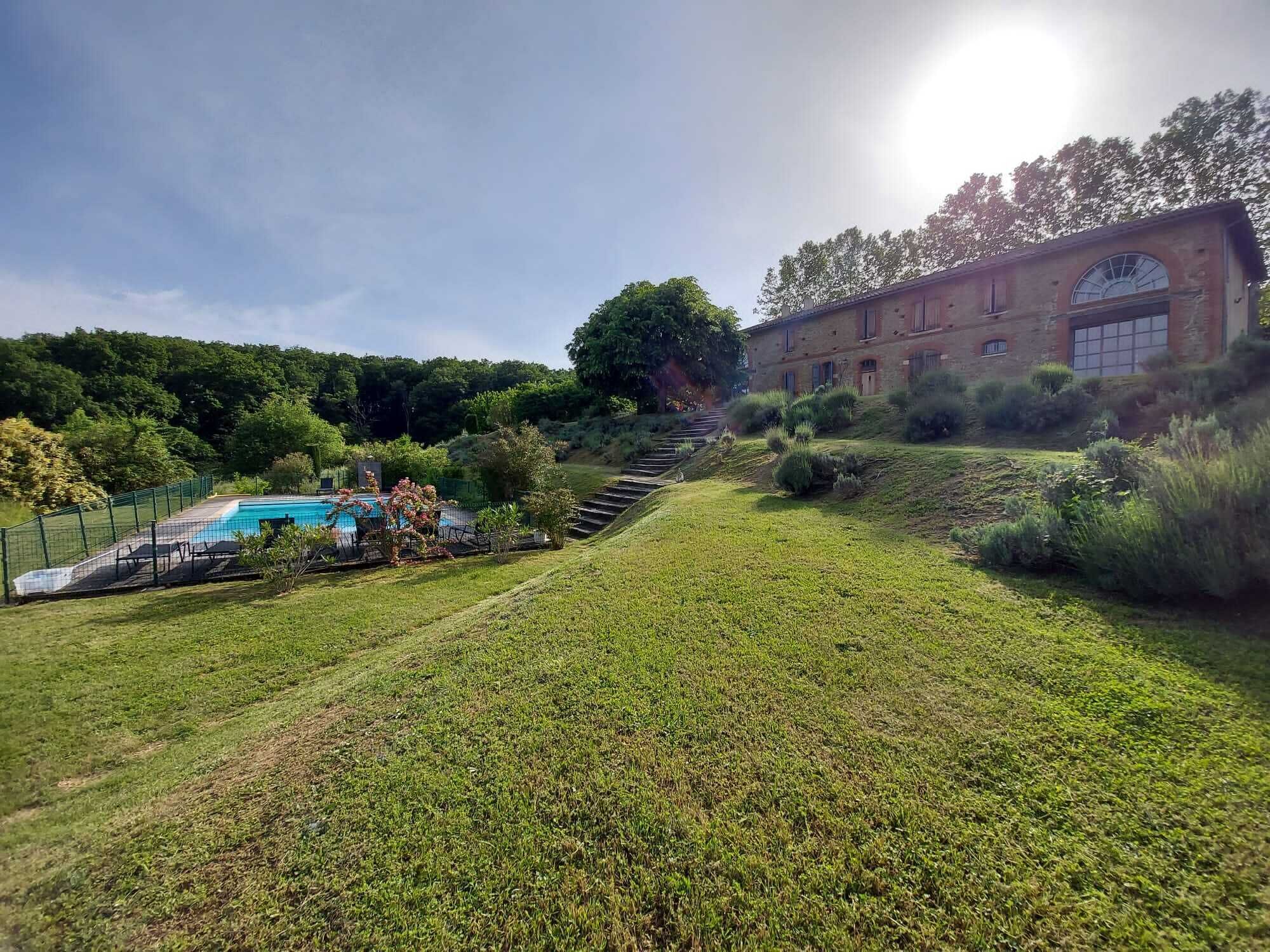 A swimming pool with a fenced deck, a grassy slope, and a building with arched windows.