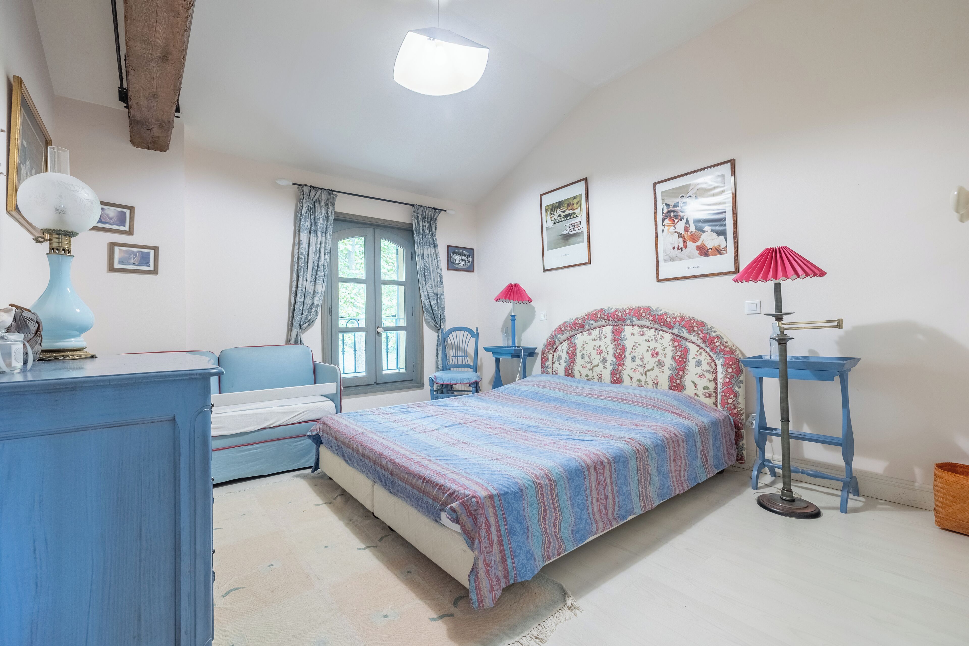 Une chambre à coucher avec un lit, un bureau, une chaise, une lampe et une fenêtre avec des rideaux.