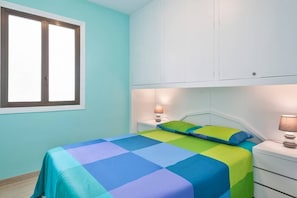 A bedroom with a bed, two bedside tables, a window, and a white wardrobe.