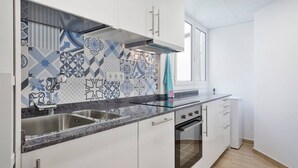 Cozinha com armários brancos, pia dupla, fogão e azulejos de parede estampados.