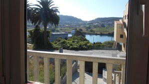 A view from a balcony with a clear sky, a palm tree, and a body of water in the distance.