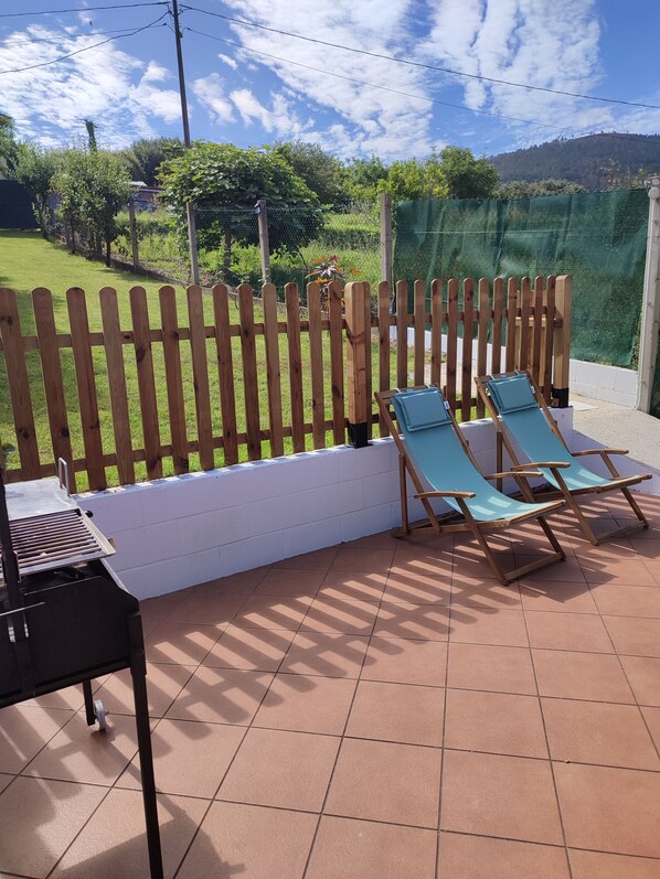 Eine Terrasse mit zwei blauen Lounge-Sesseln, einem Holzzaun und einem Grill.