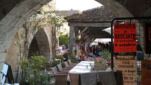 Mercado al aire libre con mesas y sillas bajo un arco de piedra.