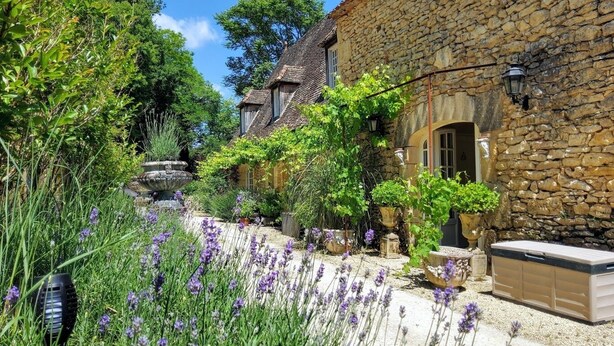 Un edificio de piedra con un jardín delantero, con plantas de lavanda y un banco de piedra.