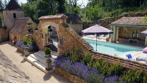 Zona de piscina de piedra con pared de piedra, una pequeña escalera y un área de estar cubierta con sombrillas.
