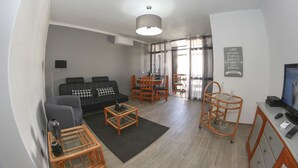 En moderne stue med sofa, sofabord og spiseområde. Der er et fjernsyn, en lampe og et skilt på væggen.