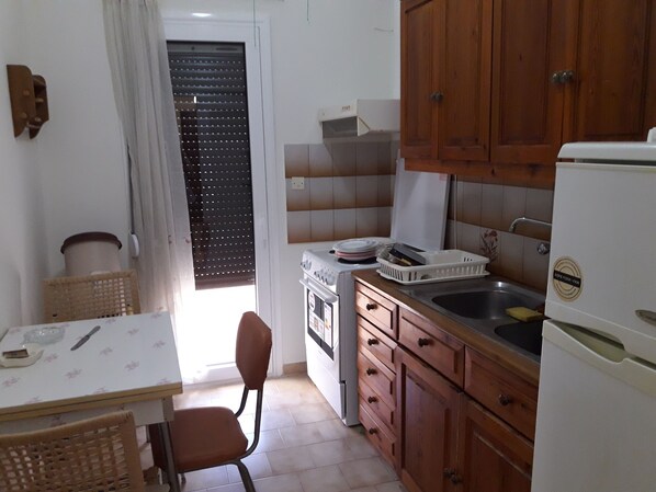 A compact kitchen with wooden cabinets, a white refrigerator, a sink, and a dining area with a table and chair.