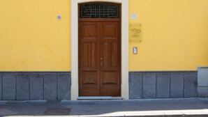 A yellow building with a brown double door, a small vent, and a plaque on the wall.