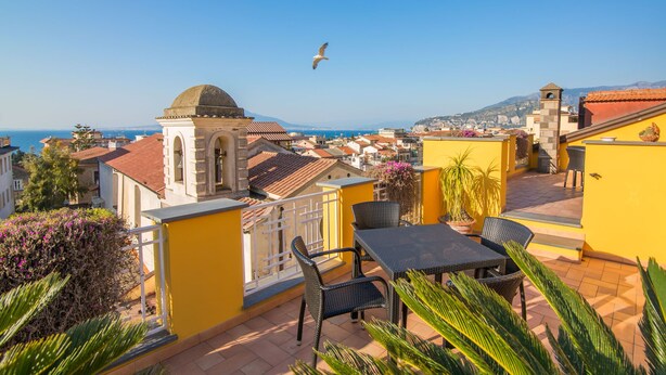A rooftop terrace with a dining area, yellow walls, and a view of the city and sea.