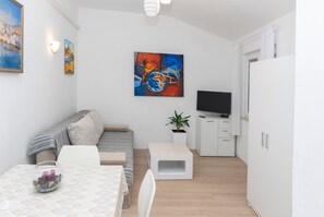 Uma sala de estar moderna com um sofá, uma televisão, um quadro e uma pequena mesa com uma vela.