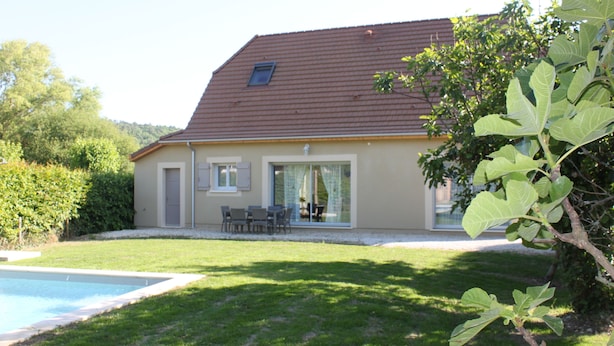 Ein Haus mit Swimmingpool, einer Terrasse mit Stühlen und einem großen Baum im Vordergrund.