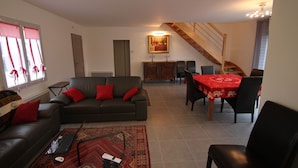 Ein Wohnzimmer mit einer Couch, einem Esstisch mit Stühlen, einer Treppe und einem Bild an der Wand.