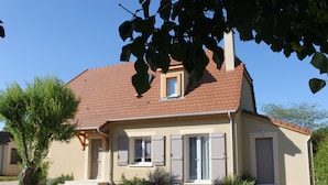 Ein zweigeschossiges Haus mit rotem Ziegeldach, einem kleinen Fenster mit Fensterläden und einer Tür mit Fenster darüber.
