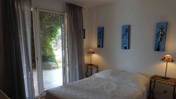 Une chambre à coucher comprenant un lit, deux tables de chevet avec des lampes, une porte-fenêtre coulissante et trois tableaux accrochés au mur.